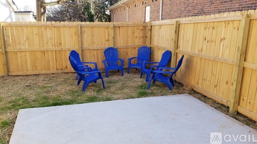 Four blue chairs are placed on a concrete slab in a backyard.