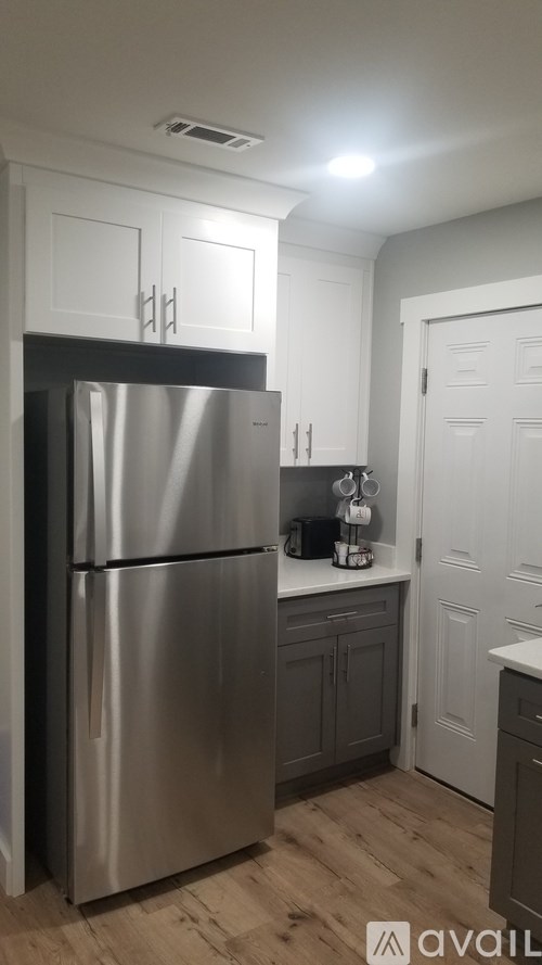 A stainless steel refrigerator in a kitchen with wooden floors and white cabinets.