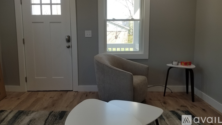 A living room with a grey couch, a white table, and a small side table with a red object on it.