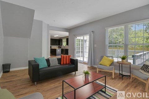 A living room with a black couch, a glass coffee table, and a balcony with a chair and a small table.