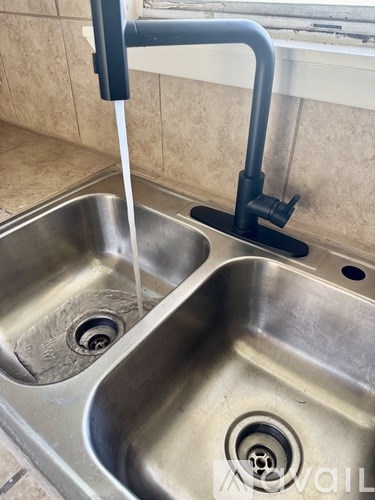 A kitchen sink with a black faucet and running water.
