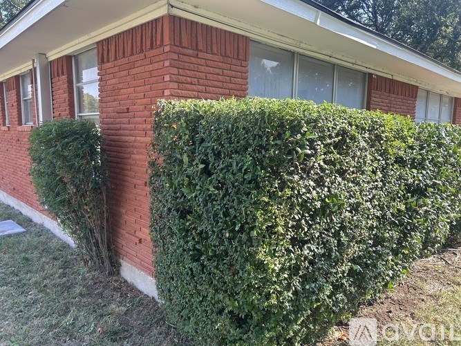 A red brick house with a green hedge in front.