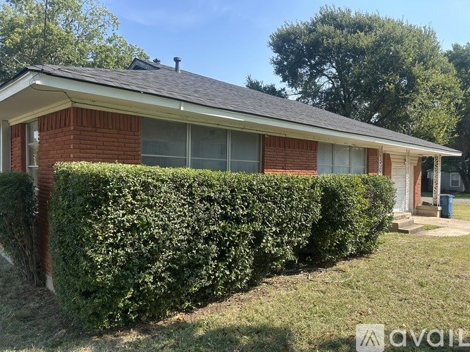 A house with a red brick facade and a grey roof with a hedge in front.