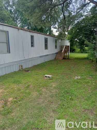 A white mobile home with a deck and a tree in the background.