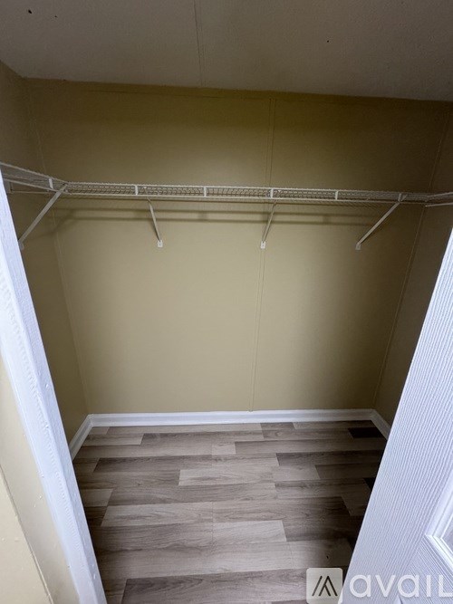 Empty room with a white closet rod and wooden floor.