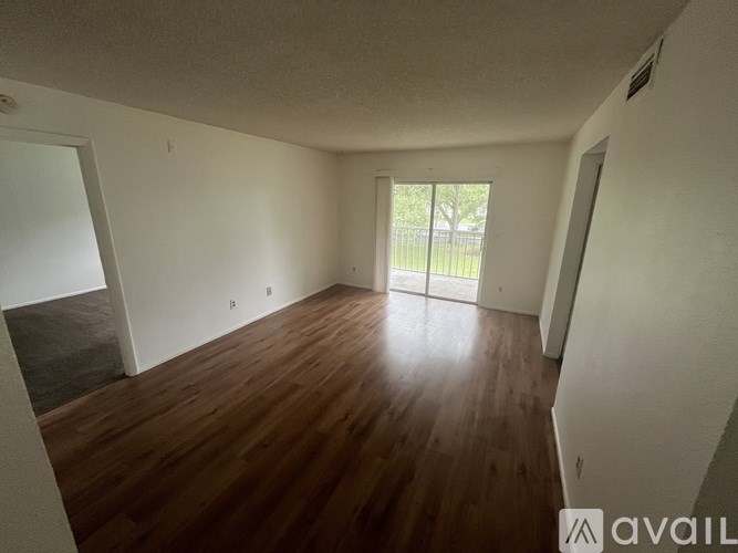 A room with wooden flooring and a sliding glass door leading to a balcony.