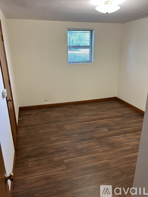 A room with wooden flooring and a window with blinds.