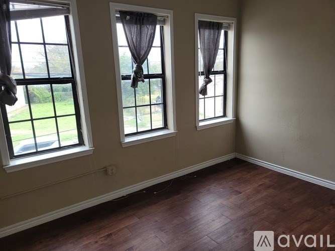 Three windows with curtains in a room with wooden floors.