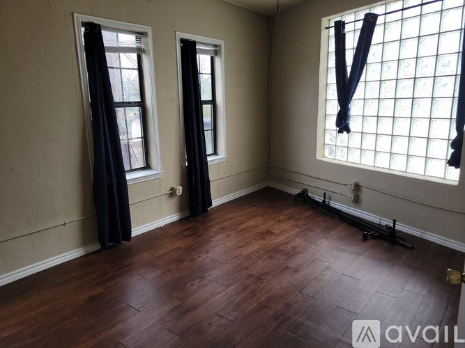 A room with wooden flooring and two windows with black curtains.