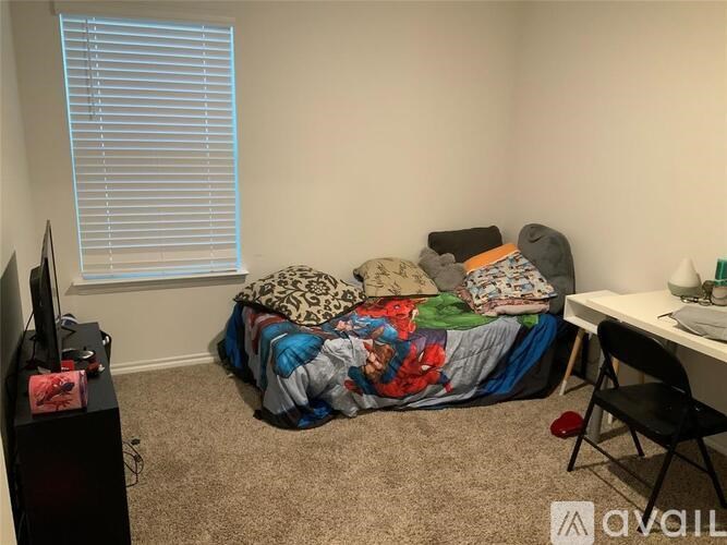 A bedroom with a bed covered in a colorful comforter, a desk with a computer, and a television.