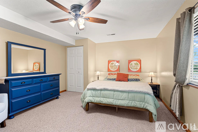 A bedroom with a blue dresser and a bed with a white comforter.