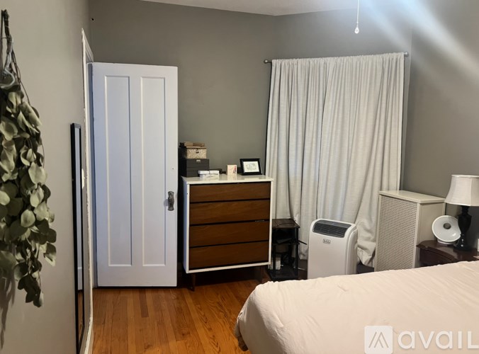 A bedroom with a bed, dresser, and window with curtains.