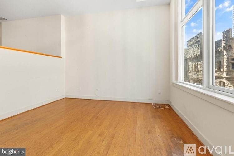 Empty room with wooden floors and a window overlooking a cityscape.