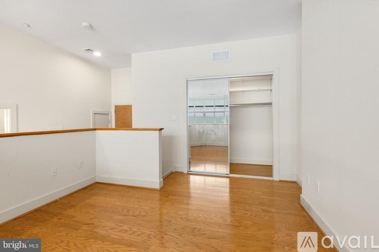 A room with wooden floors and white walls, with a doorway leading to another room.