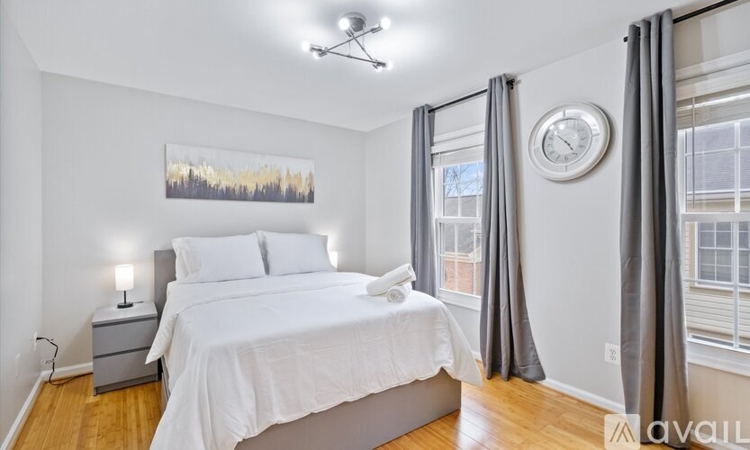 A bedroom with a large bed, a nightstand with a lamp, a clock, and a painting on the wall.