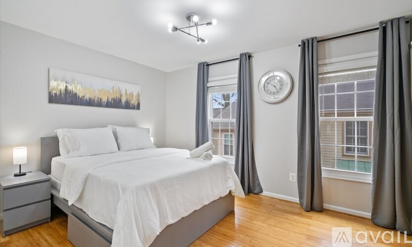 A bedroom with a large bed, a nightstand, a clock, and a painting on the wall.