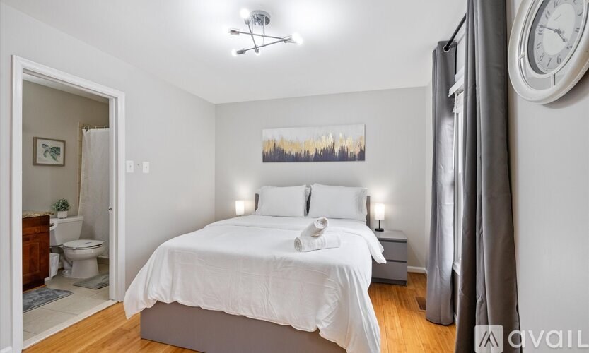 A bedroom with a large bed, a painting on the wall, and a clock on the wall.