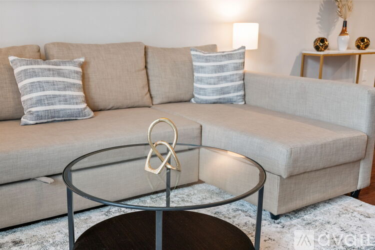 A living room with a beige sofa, a glass coffee table, and a round wooden table.
