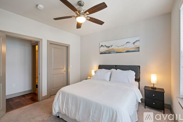 A bedroom with a large bed, a ceiling fan, and a painting on the wall.