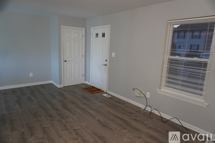 A room with a door, a window with blinds, and a wooden floor.
