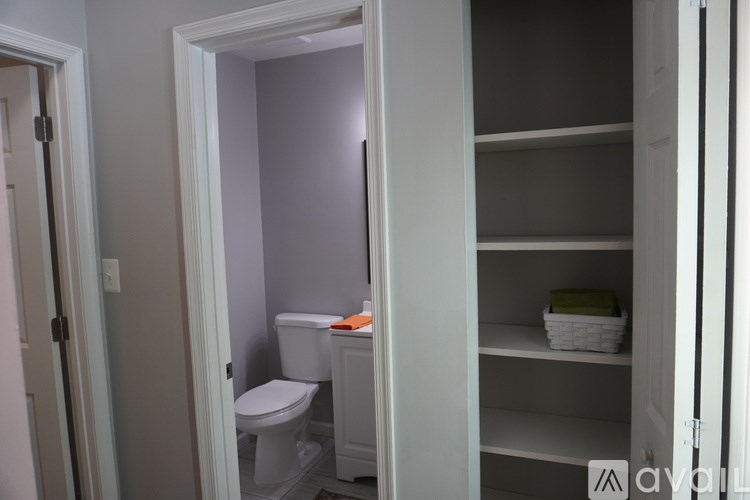A white toilet sits in a small bathroom next to a white shelf.