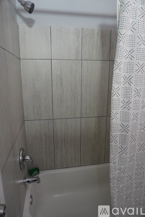 A shower with a white tub and a shower curtain with a pattern.