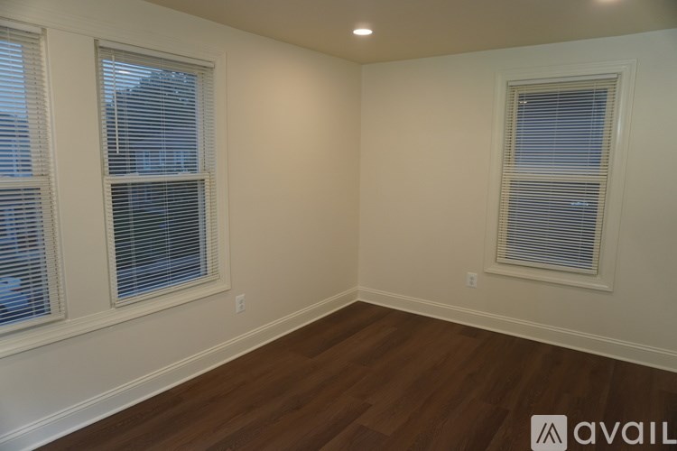 A room with wooden floors and two windows with blinds.