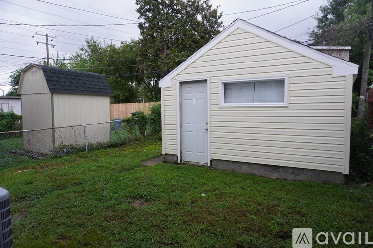 A small beige shed with a white door and a window is situated in a grassy area.