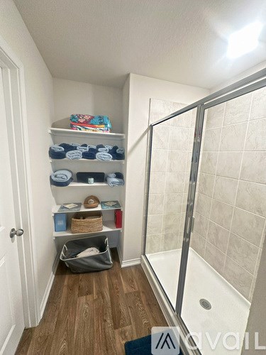 A bathroom with a walk in shower and a shelf with towels and baskets.