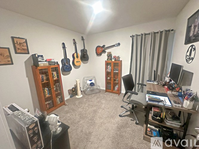 A room with a desk, chairs, and guitars on the wall.