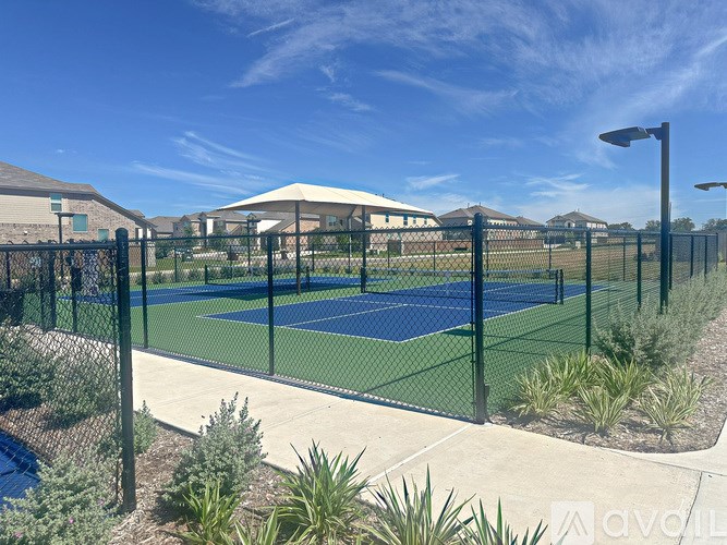 A tennis court surrounded by a black fence and green plants.