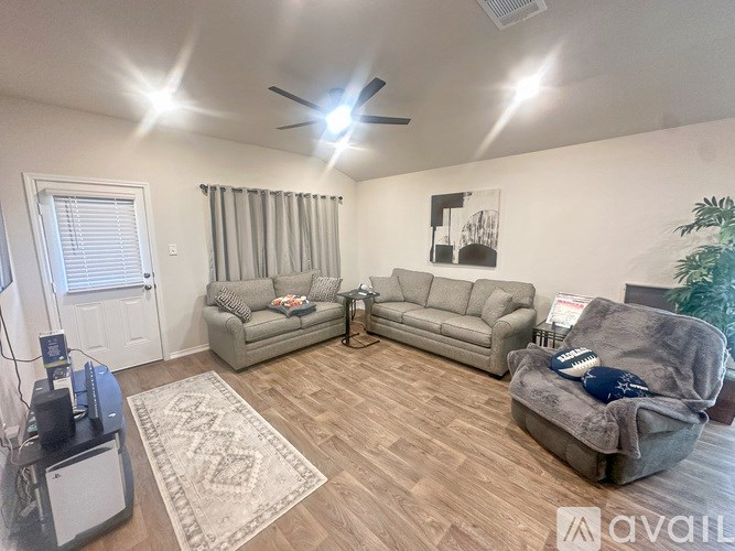 A living room with a grey couch, a grey sofa, a rug, a ceiling fan, and a plant.