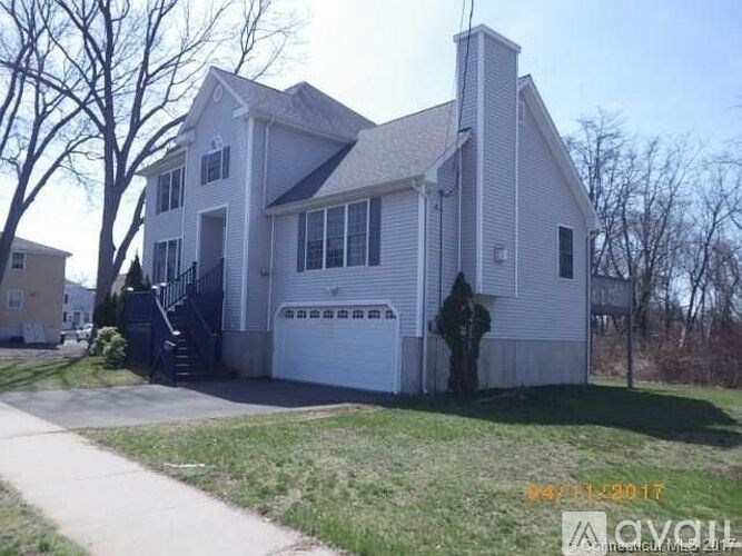 A white house with a black gate and a tree in front.