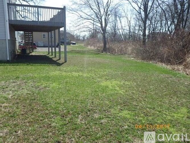 A house with a deck and a carport is surrounded by a grassy area.