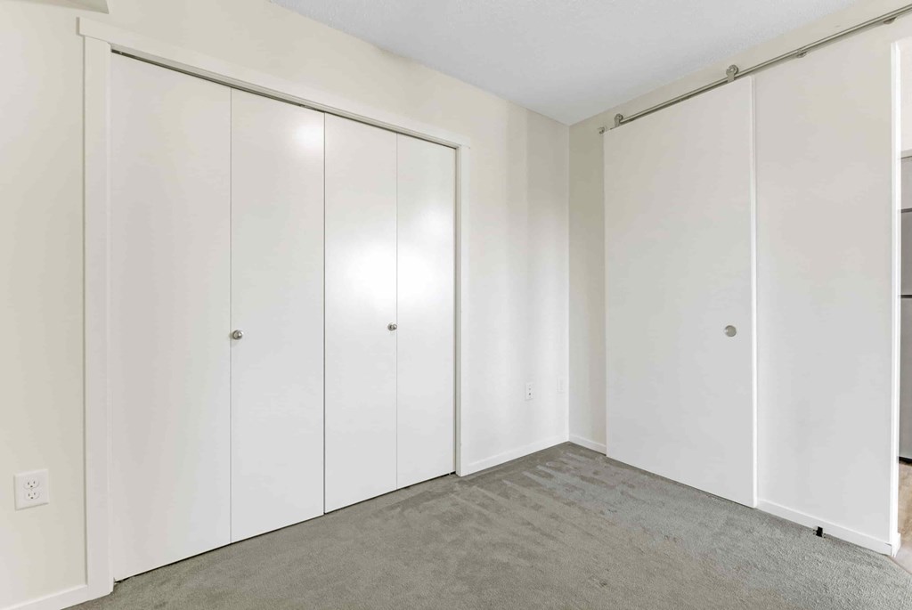 A room with white cupboards and grey carpet.