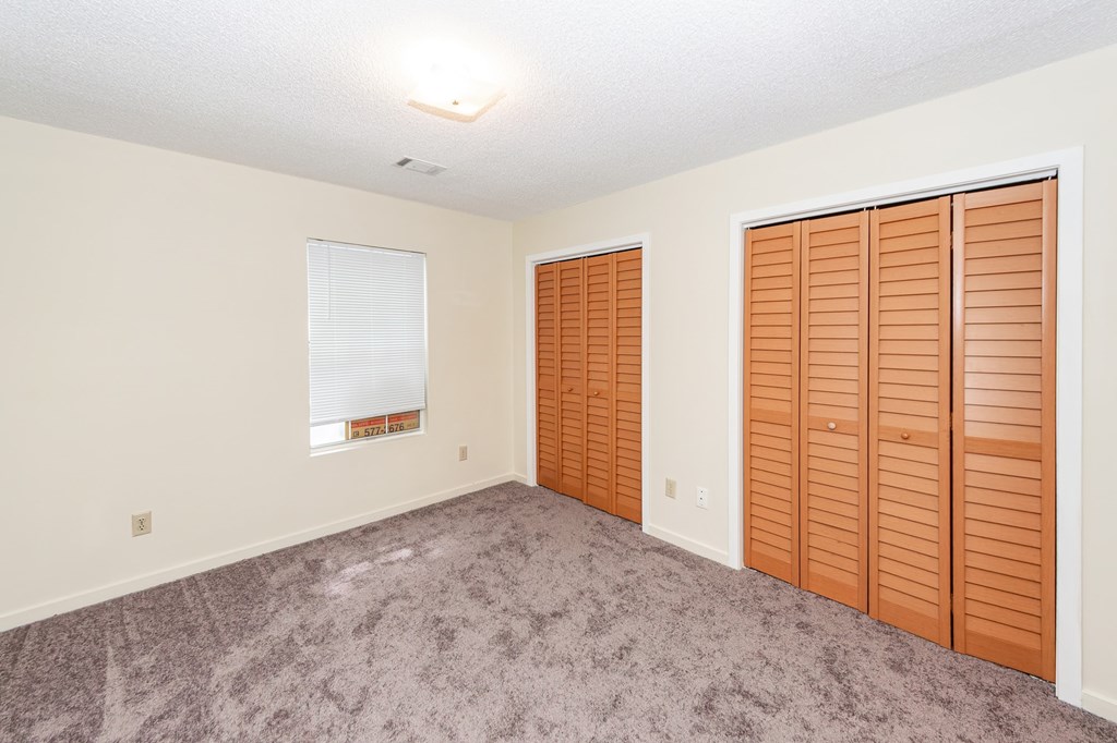 A room with a carpeted floor and a window with blinds.