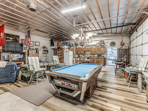 A pool table is in the middle of a room with a wooden floor and a ceiling with exposed pipes.