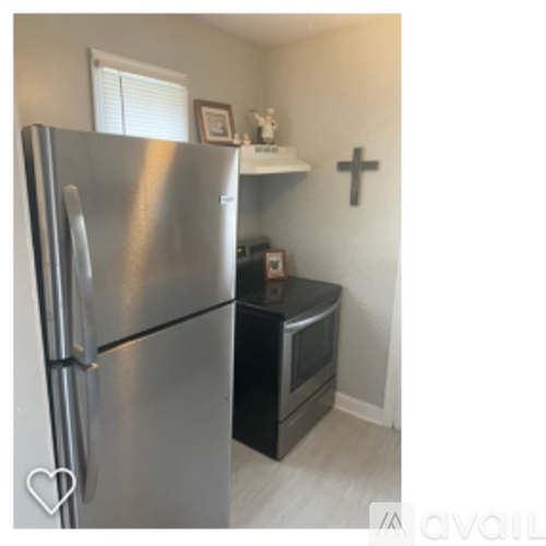 A stainless steel refrigerator in a kitchen with a black countertop and a white wall with a cross symbol.