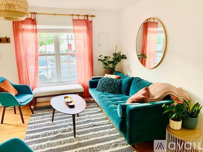 A living room with a green couch, a blue chair, a coffee table, and a round mirror on the wall.