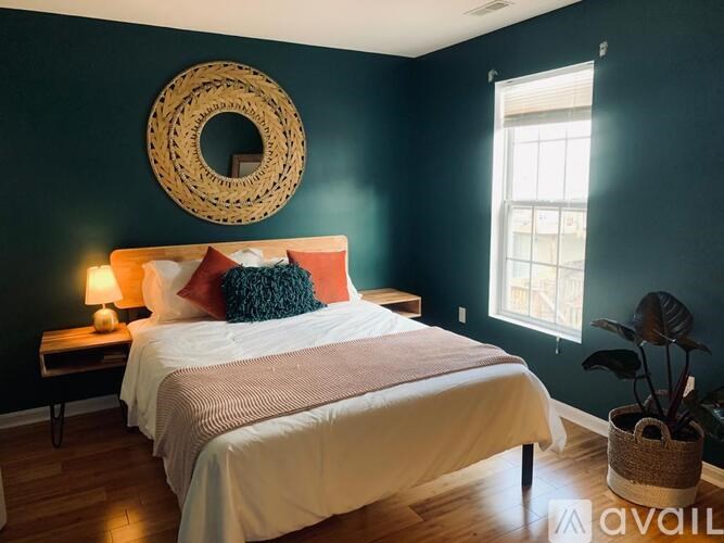 A bedroom with a bed, a wicker basket, a table with a lamp, and a window.