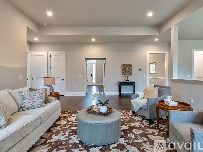 A living room with a white couch, a grey ottoman, and a patterned rug.