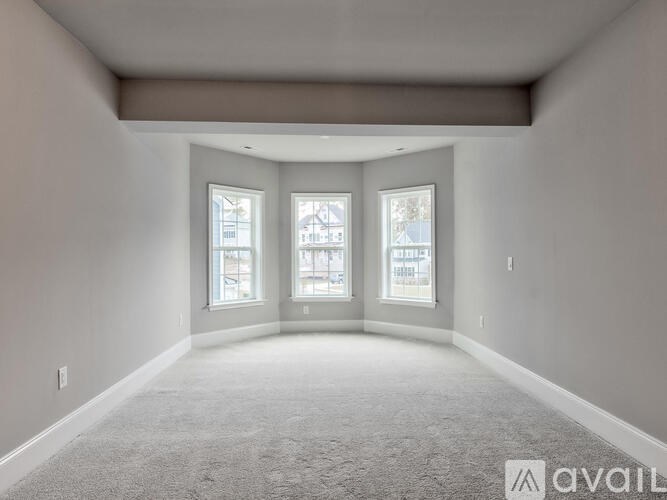 A spacious room with carpeted floor and three windows.