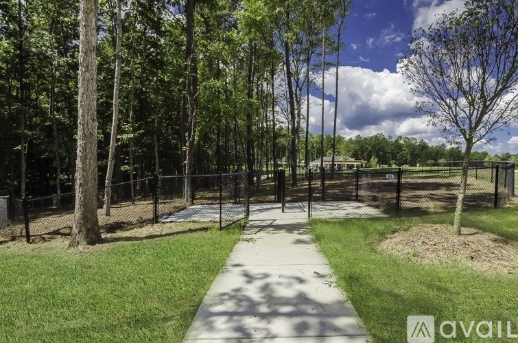 A park with a walking path, trees, and a fence.