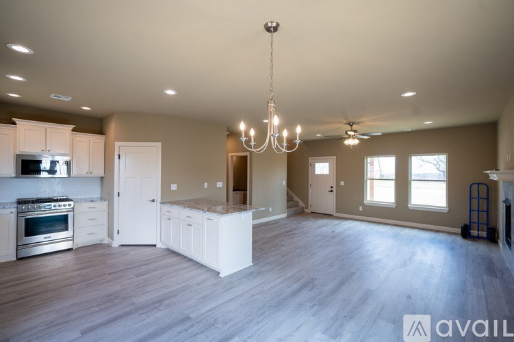 A large, empty room with a kitchen area to the left and a staircase to the right.
