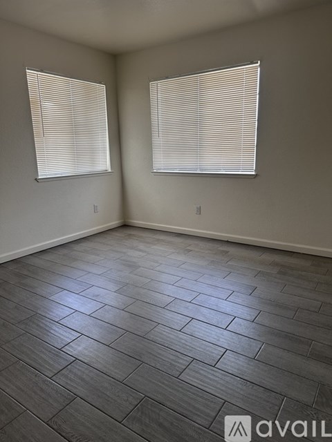 A room with wooden flooring and two windows.