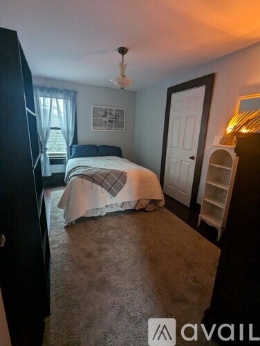 A bedroom with a bed, dresser, and a window with curtains.