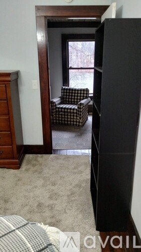 A black refrigerator stands in a room with a checkered chair and a window.