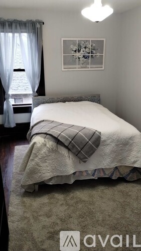 A bedroom with a bed covered in a white comforter and a grey blanket.