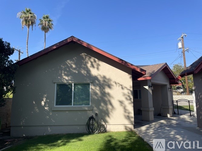 A house with a red roof and a white wall with a window and a hose on the ground.