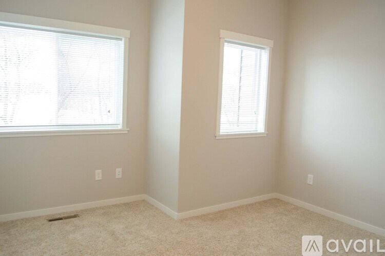 A room with two windows and carpeted flooring is available for rent.